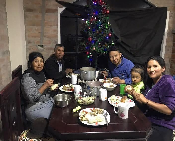 An intergenerational indigenous Cayambe family eating a meal at a table and smiling warmly at the camera