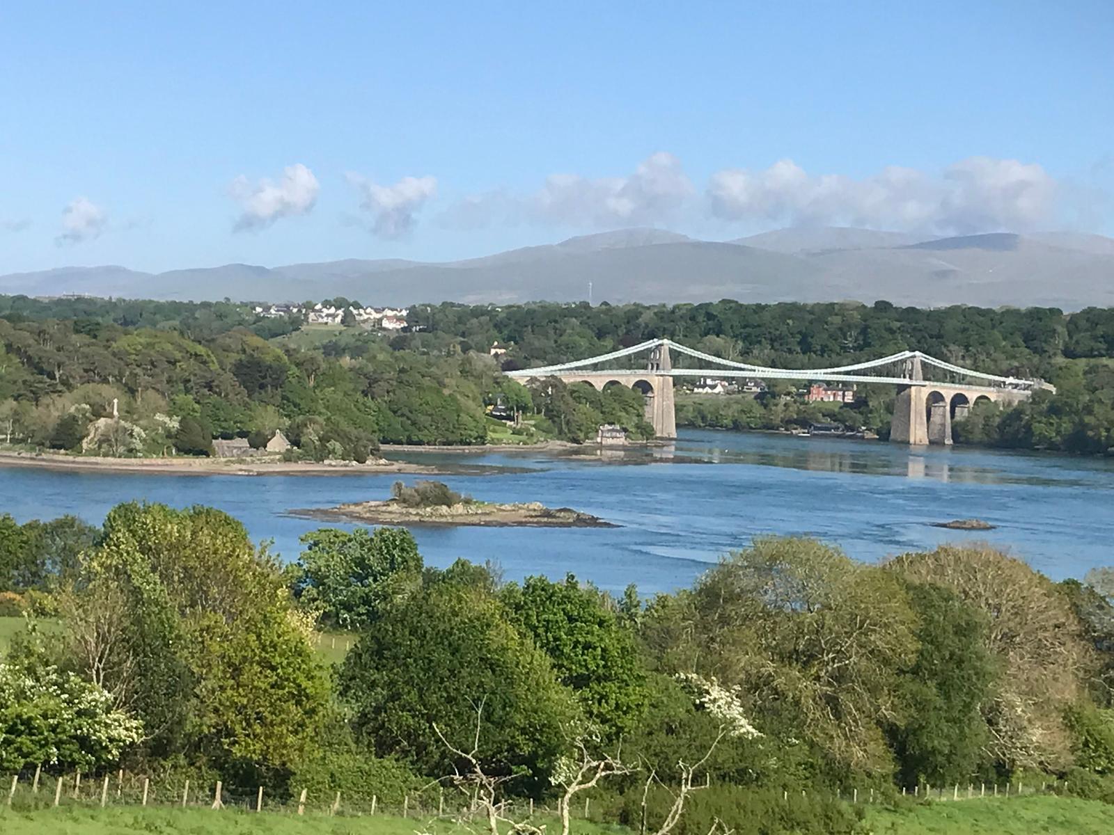 Terfyn cae, coetir llydanddail, Y Fenai, Eglwys Sant Tysilio, Pont Grog y Borth, a Bangor yn y pellter canol gyda mynyddoedd Eryri yn y cefndir.