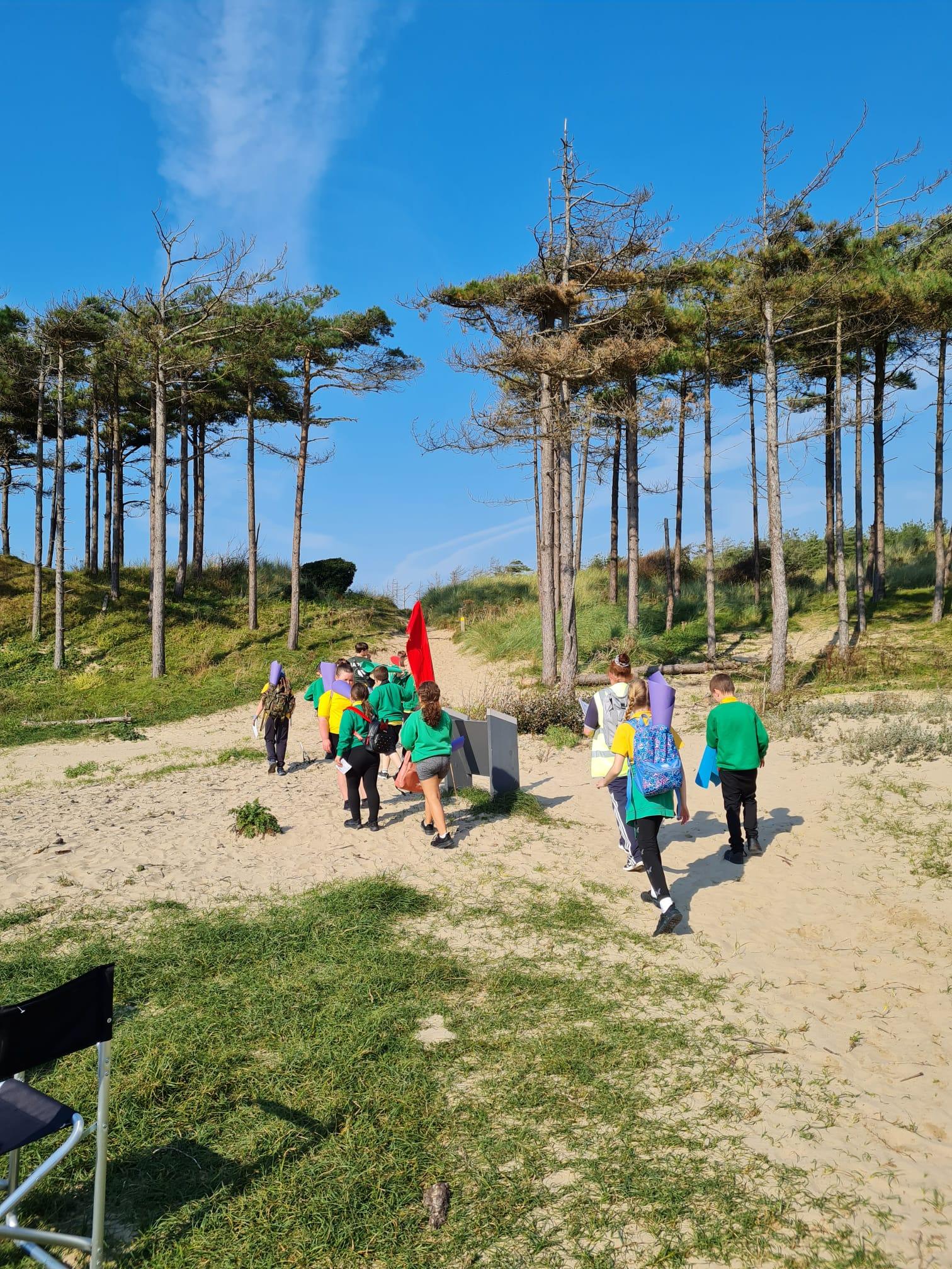 A group of children walk purposefully through the sandy paths of the beach.
